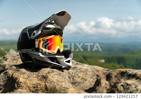 Side view of a full face black and white downhill mountain bike helmet. Extreme sports gear, against a backdrop of nature and a mountain landscape with cumulus clouds Side view of a full face black and white downhill mountain bike helmet. Extreme sports gear, against a backdrop of nature and a mountain landscape with cumulus clouds 128421257