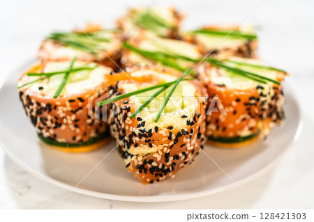 A beautiful arrangement of smoked salmon jumbo cream cheese rolls served on a plate. The rolls are evenly garnished with fresh chives and feature a crunchy sesame seed coating. This dish is a perfect 128421303