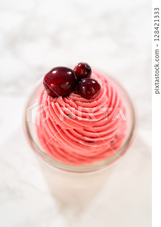 A swirl of vibrant cranberry buttercream piped into a glass jar and topped with fresh cranberries. This creamy, tart frosting is perfect for cookies, cakes, and holiday desserts. 128421333