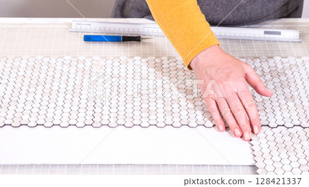 In the process of mounting peel and stick mosaic tiles onto a foam board, perfect for enhancing a food photography studio's aesthetic. 128421337