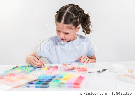Little girl enjoys crafting colorful bracelets with vibrant clay beads set. 128421339