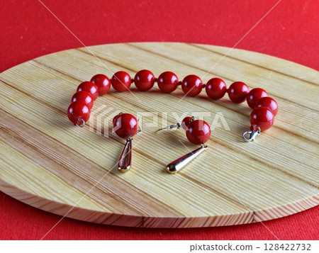 Set of bracelet and earrings made of shiny red coral on wooden background. Close-up. Set of bracelet and earrings made of shiny red coral on wooden background. Close-up. 128422732