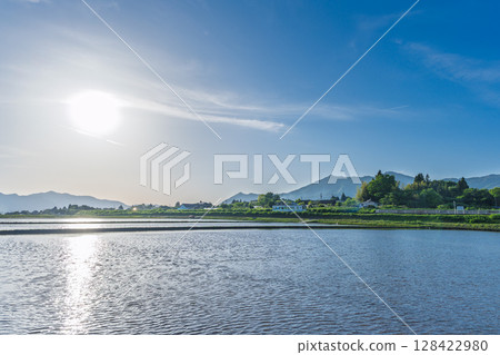 A rural landscape lit by sunlight and with the Aso mountain range in the background (Aso, Minamiaso Village) 128422980