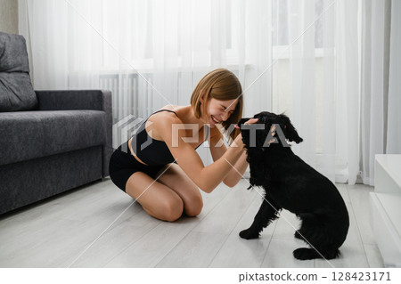 Happy young woman cuddling playful black cocker spaniel puppy indoors. 128423171