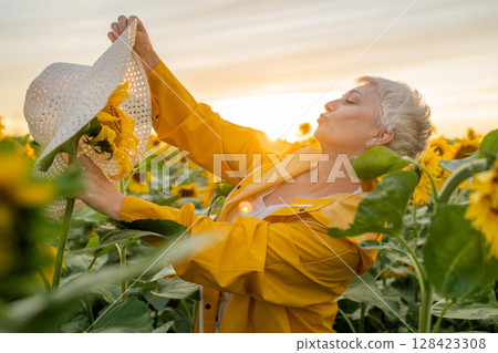 A Joyful Woman playfully puts hat on sunflower in a Field of Sunflowers is Celebrating the Natural Beauty Around Her A Joyful Woman playfully puts hat on sunflower in a Field of Sunflowers is Celebrating the Natural Beauty Around Her 128423308
