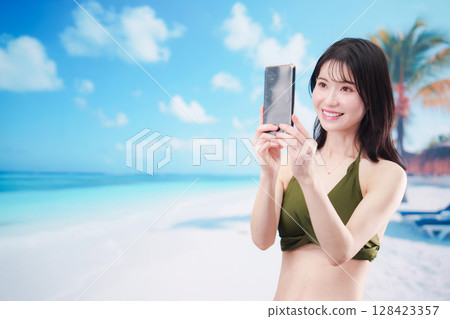 一位身穿泳衣的年輕女子在陽光明媚的海灘上用智慧型手機自拍 一位身穿泳衣的年輕女子在陽光明媚的海灘上用智慧型手機自拍 128423357