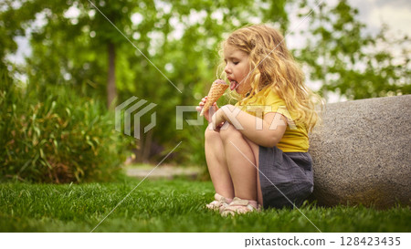Final lick. Little girl crouching on grass enjoying ice cream outdoors 128423435