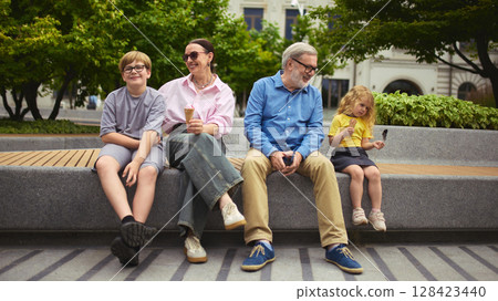 Family sitting on bench enjoying ice cream outdoors 128423440