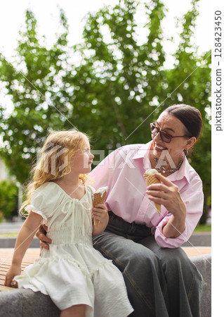 Grandmother and girl laugh together eating ice cream. 128423450