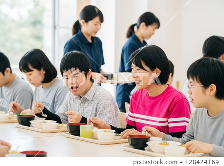 一位面帶微笑的女護理員在殘疾人設施內為殘疾人士提供餐食。提供食物、午餐時間、學校午餐、餐點、樂趣 128424169