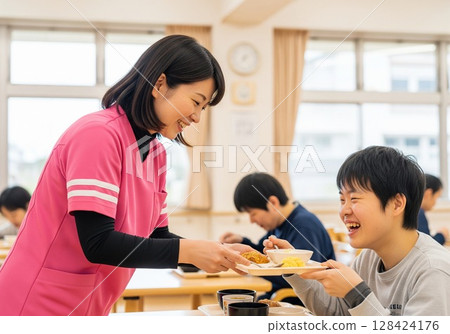 Smiling female caregiver serving meals at a facility for people with disabilities. Serving food, lunchtime, school lunch, meal, fun 128424176