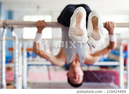 Gymnast performs complex tricks on horizontal bar in gym Gymnast performs complex tricks on horizontal bar in gym 128424408