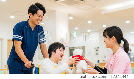 推著輪椅。男女照顧者面帶微笑地與一位殘障人士互動。使用者的笑容。 128424443