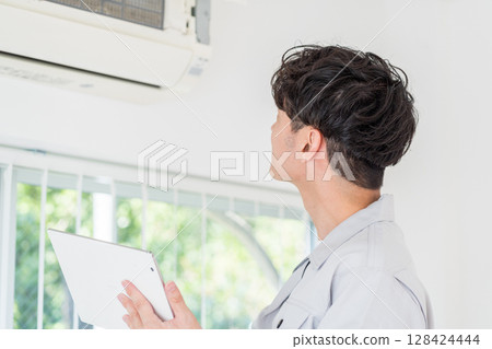 A male worker checks the operation of an air conditioner. 128424444