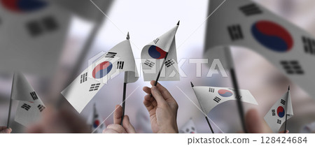 South Korean flags in their hands on a blurred urban background South Korean flags in their hands on a blurred urban background 128424684