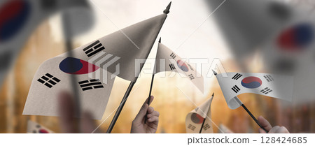 South Korean flags in their hands on a blurred urban background South Korean flags in their hands on a blurred urban background 128424685