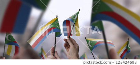 Comoros flags in their hands on a blurred urban background Comoros flags in their hands on a blurred urban background 128424698