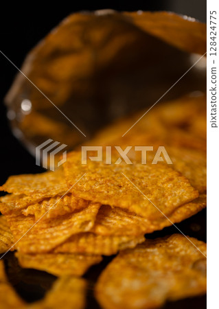 Golden savory seasoned crispy potato chips spilling from an open foil snack bag, embodying indulgent enjoyment, casual eating, and festive party food Golden savory seasoned crispy potato chips spilling from an open foil snack bag, embodying indulgent enjoyment, casual eating, and festive party food 128424775