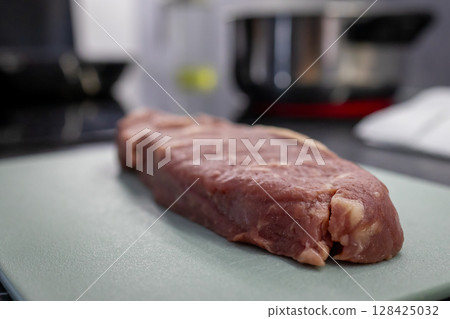 Fresh raw beef steak on a light green cutting board, symbolizing healthy home cooking and nutritious meal preparation in a culinary setting 128425032