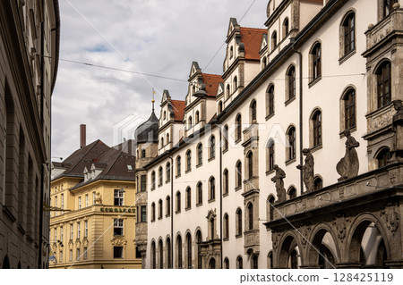 Historic Architecture Near Marienplatz Munich: Ornate Facades And Baroque Dome Along Narrow Street With Dramatic Sky Historic Architecture Near Marienplatz Munich: Ornate Facades And Baroque Dome Along Narrow Street With Dramatic Sky 128425119