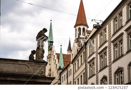 Historic Toy Museum In Munich Near Marienplatz: Old Tower With Red Roof And Green Spire Framed By Stone Arch Against Dramatic Cloudy Sky Historic Toy Museum In Munich Near Marienplatz: Old Tower With Red Roof And Green Spire Framed By Stone Arch Against Dramatic Cloudy Sky 128425287
