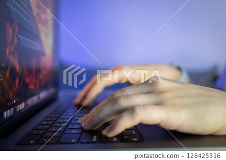 Human hands actively typing on a laptop keyboard with a glowing screen, representing remote work, digital communication, and focused productivity in a modern tech setting 128425516