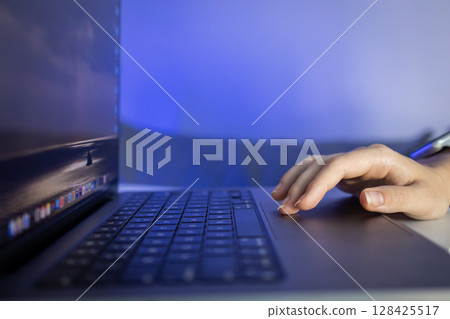 An anonymous user's hand navigates a laptop's trackpad, symbolizing effective remote work, engaged digital learning, and streamlined technological interaction at night 128425517