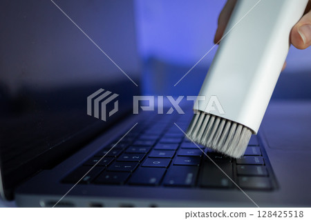 A white cleaning brush diligently sweeps dust off a sleek laptop keyboard, promoting essential electronic device care and regular maintenance for improved longevity 128425518
