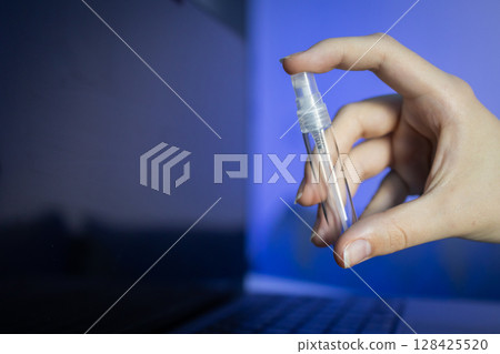 Hand holding a transparent spray bottle, ready to clean a dark laptop screen, symbolizing essential electronics hygiene and careful device maintenance Hand holding a transparent spray bottle, ready to clean a dark laptop screen, symbolizing essential electronics hygiene and careful device maintenance 128425520