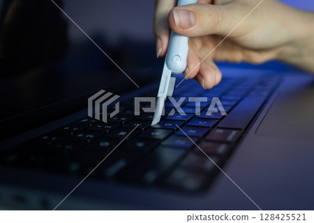 Hand cleaning a laptop keyboard with a specialized tool, promoting electronic device maintenance and hygiene in a digital workspace 128425521