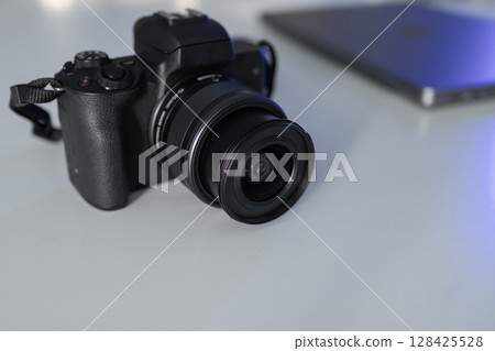 Professional black mirrorless camera with a lens resting on a clean white desk, symbolizing modern digital photography and videography for content creation 128425528