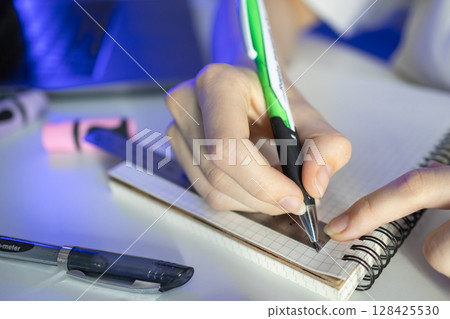 Student's hand diligently using a green pen and ruler on a grid notebook, illustrating academic precision, focused learning, and effective study methods 128425530