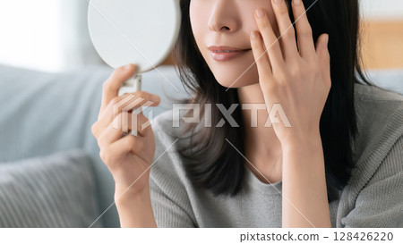 A woman checking her skin in the mirror 128426220
