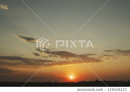 Beautiful sunset in the city with clouds and sun rays. The sun sets over the city. 128426222