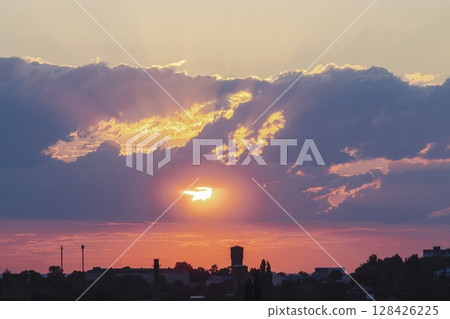 Beautiful sunset in the city with clouds and sun rays. The sun sets over the city. 128426225