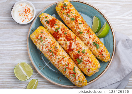 Elotes mexican street corn cob covered in spices and cheese being served on plate 128426556
