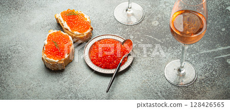 Small metal plate with red salmon caviar, two caviar toasts canape, two glasses of champagne top view on grey concrete background, festive luxury delicacy and appetizer Small metal plate with red salmon caviar, two caviar toasts canape, two glasses of champagne top view on grey concrete background, festive luxury delicacy and appetizer 128426565