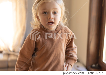 A three-year-old boy with blond curly hair is jumping on the couch at home 128426714