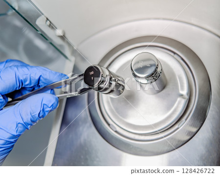 A operator's hand is holding steel calibration weight to place on the analytical balance.. A operator's hand is holding steel calibration weight to place on the analytical balance.. 128426722
