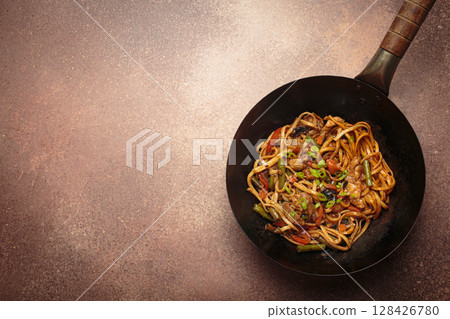 Asian style stir fry noodles with chicken and vegetables in a black wok pan with chopsticks, space for text Asian style stir fry noodles with chicken and vegetables in a black wok pan with chopsticks, space for text 128426780