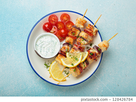 Grilled chicken skewers with lemon wedges, cherry tomatoes and yogurt sauce top view Grilled chicken skewers with lemon wedges, cherry tomatoes and yogurt sauce top view 128426784