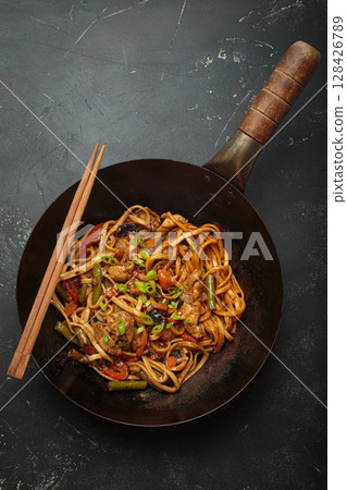 Asian style stir fry noodles with chicken and vegetables in a black wok pan with chopsticks 128426789