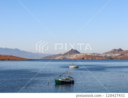 Boats float on calm blue waters, with coastal towns and rugged mountains under a clear sky, showcasing a serene Mediterranean landscape. High quality photo Boats float on calm blue waters, with coastal towns and rugged mountains under a clear sky, showcasing a serene Mediterranean landscape. High quality photo 128427431