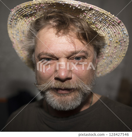 A man with facial hair in a straw hat and fedora, wrinkles on his jaw 128427546