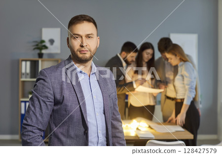 Serious Businessman Portrait With Office Team Working In Background Serious Businessman Portrait With Office Team Working In Background 128427579