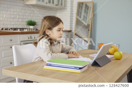 Child doing homework with tablet, paper notebook, learning online on school lesson, sitting at home Child doing homework with tablet, paper notebook, learning online on school lesson, sitting at home 128427600