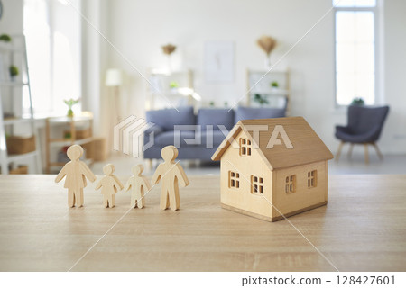 Wooden figures of family and toy house standing at table in empty living room at home. 128427601