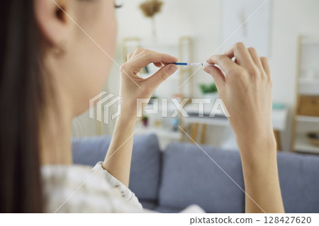 Close up of young woman looking at positive pregnancy test with two stripes. Family planning concept 128427620