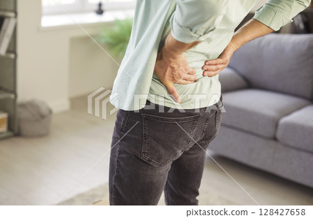 Cropped portrait of man suffering from backache standing in living room at home. Cropped portrait of man suffering from backache standing in living room at home. 128427658
