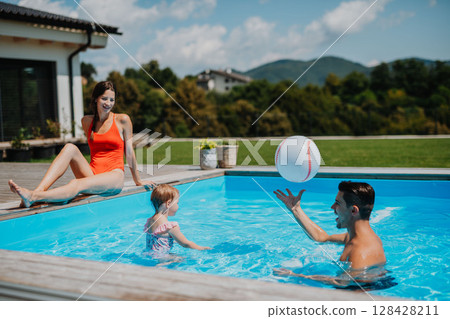 Young family with small daughter in swimming pool outdoors in backyard garden. 128428211
